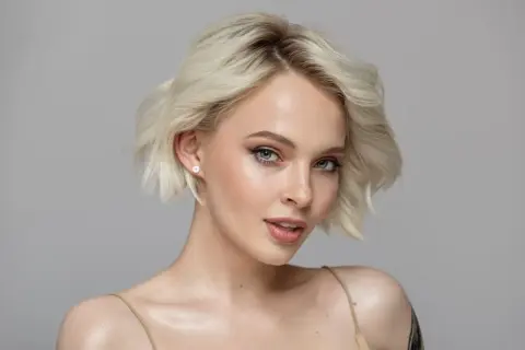 Mujer joven con piel blanca, ojos marrones y cabello rubio platino.