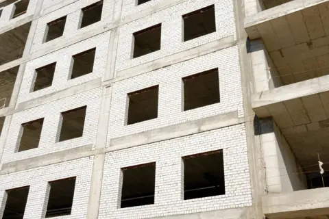 Fachada monocapa blanco de edificio en construcción, con ventanas vacías y balcones de hormigón.