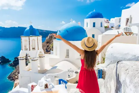 Santorini w kwietniu zachwyca! Kobieta w czerwonej sukience i kapeluszu cieszy się idealną pogodą, podziwiając białe domy i niebieskie kopuły.