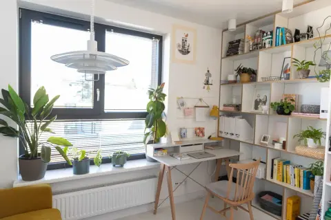 Jasny gabinet w domu z biurkiem, regałem pełnym książek i roślin. Inspiracje do aranżacji domowego biura.