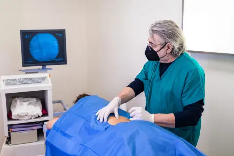 Un médecin réalise une infiltration du dos guidée par imagerie. Le patient est allongé, couvert d'un drap bleu.