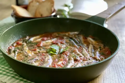 Un saporito bagnun di acciughe in padella, con pomodoro e prezzemolo, pronto per essere gustato con pane tostato.