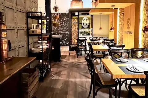 Interior de un bistro bar con mesas puestas, sillas de madera oscura y decoración industrial.