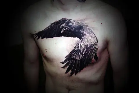 Impresionante tatuaje de cuervos en el pecho, con un ave en pleno vuelo, alas extendidas y pico abierto.