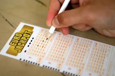 Dłoń z ołówkiem zaznacza liczby na kuponie Eurojackpot.