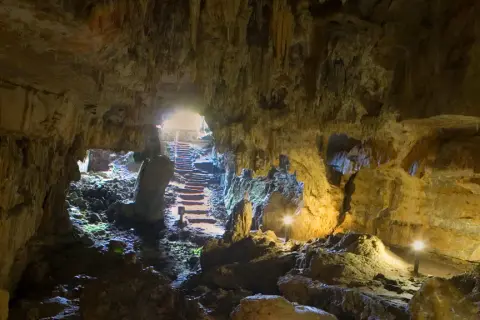 Interior de la cueva del Pindal, con estalactitas, rocas y escaleras iluminadas que conducen a la salida.