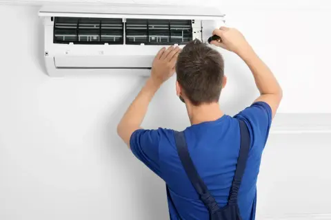 Tecnico con cacciavite apre un condizionatore per manutenzione. Il significato di "heat condizionatore" è la sua capacità di riscaldare.