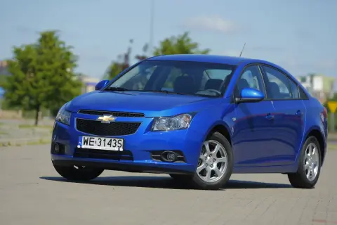 Błękitny Chevrolet Cruze 1.8 benzyna zaparkowany na placu.