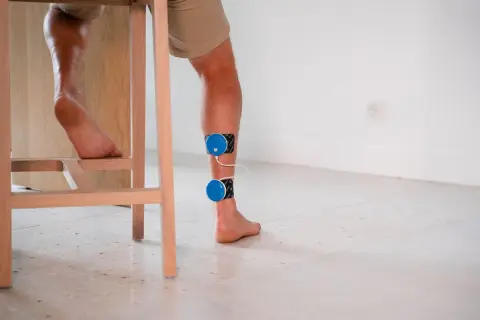 Un coureur souffrant de douleur au tendon d'Achille utilise un appareil d'électrostimulation pour soulager sa blessure.