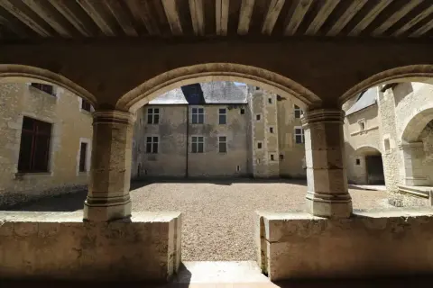 Vue d'une cour intérieure de château, avec des arches en pierre et un sol gravillonné. Une fougère sur bièvre, symbole discret de la nature, s'épanouit peut-être dans un coin caché.