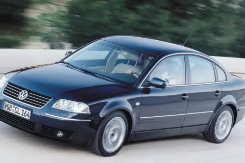 Ciemnoniebieski VW Passat W8 z jasnym wnętrzem mknie po drodze, za kierownicą siedzi mężczyzna.