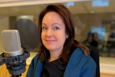 Anna Borg ler mot kameran i en inspelningsstudio, med en mikrofon framför sig.