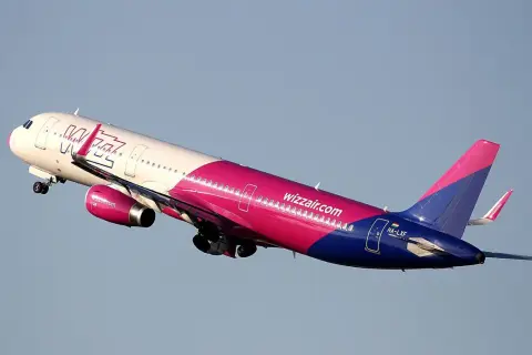 Samolot Wizz Air w różowo-niebieskich barwach wznosi się na tle błękitnego nieba.
