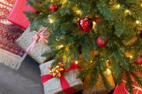 Idée tuto sapin de noël : des cadeaux emballés sous un sapin décoré de boules rouges et de guirlandes lumineuses.