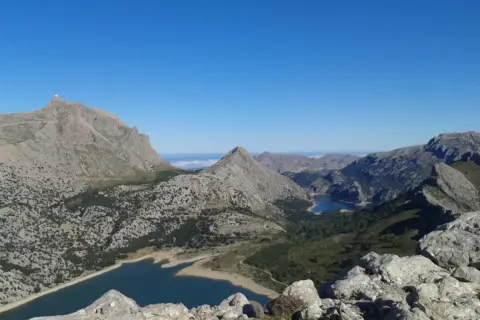 Vistas impresionantes desde el Puig de sa Rateta, con embalses y montañas escarpadas bajo un cielo azul.