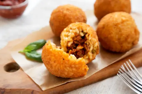 Arancini dorés et croustillants, une recette sicilienne à déguster. Un est un arancino ouvert révèle sa garniture savoureuse.
