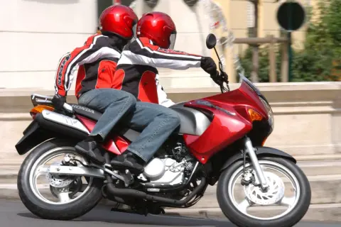 Dwie osoby w czerwonych kaskach i kurtkach jadą na czerwonym motocyklu. To świetna kategoria a1 dla miłośników wolności.