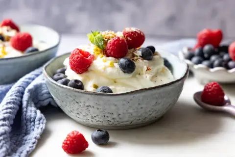 Cremiger frozen Joghurt mit frischen Himbeeren und Blaubeeren, garniert mit Minze und Nüssen. Ein erfrischender Genuss.