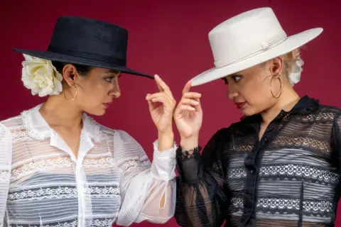 Dos mujeres con sombreros de ala ancha y blusas de encaje, listas para conciertos flamenco Zaragoza.