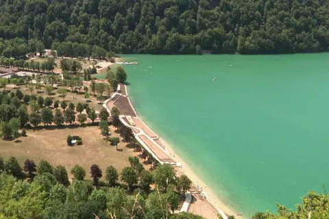 Vue aérienne d'un magnifique lac aux eaux turquoise, idéal pour la baignade. Des plages aménagées bordent la rive, entourées de verdure et d'arbres.
