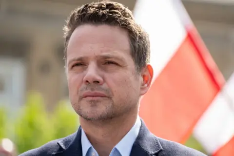 Rafał Trzaskowski, którego wiek jest często dyskutowany, na tle biało-czerwonych flag.