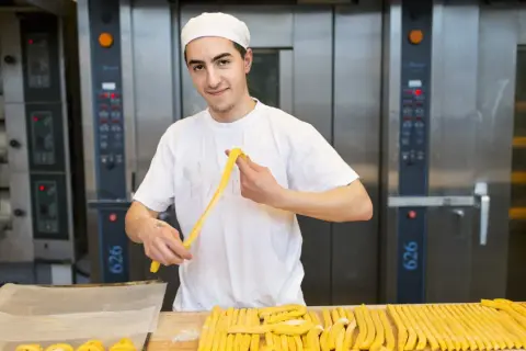 Bagare jobbar på långfredagen och formar deg till bröd framför stora ugnar.