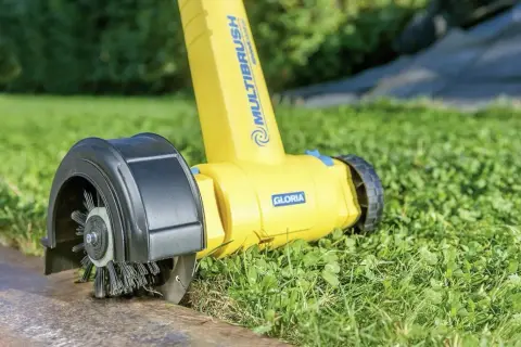 Żółta obcinarka do krawędzi trawnika z obrotową szczotką, pracująca na trawniku przy betonowym obrzeżu.