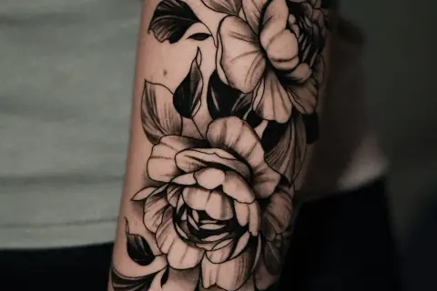 Un primer tatuaje de peonías en blanco y negro, detallado y artístico, adornando un brazo.