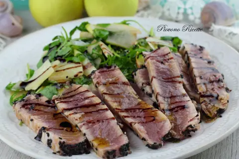 Deliziosa tagliata di tonno scottata, cosparsa di semi di sesamo nero, servita con un'insalata fresca di rucola e scaglie di parmigiano.