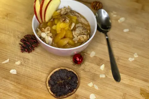 Schüssel mit Bratapfel Porridge, garniert mit Apfelscheiben und Mandelblättchen. Ein festlicher Genuss für kalte Tage.