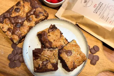 Pyszne brookies z kawałkami czekolady, obok maliny i opakowanie ciemnej czekolady.