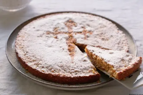 Tarta de Santiago, espolvoreada con azúcar glas, con una porción servida.