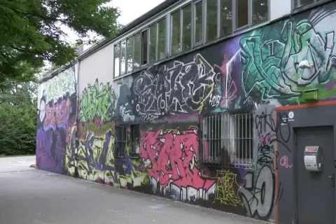 Bunte Graffiti-Kunst bedeckt die Wand eines Gebäudes, mit Fenstern und einer Tür.