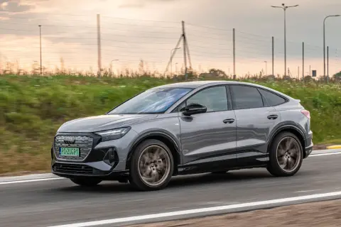 Szary Audi Q4 Sportback sunie po drodze, otoczony zielenią i zachodzącym słońcem.