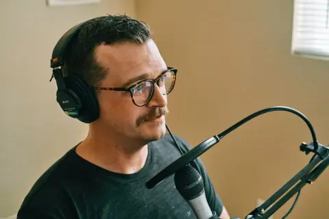Mężczyzna w słuchawkach i okularach z wąsami ustawia mikrofon.