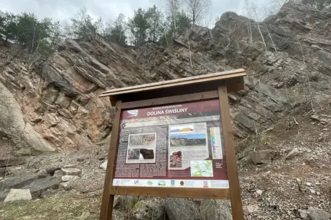 Tablica informacyjna przy skalnych ścianach w Dolinie Świniły, dawnych dołach biskupich kanion.