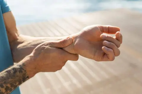 Mann hält sich das Handgelenk, da er Handgelenk schmerzen hat.