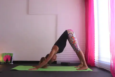 Donna in posizione di Urdhva Mukha Svanasana su un tappetino verde, con leggings colorati e uno sfondo rosa.