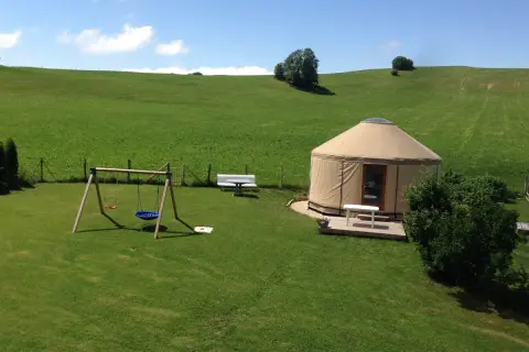 Une yourte confortable vous attend pour un séjour paisible en pleine nature, location yourte Jura. Balançoire et bancs invitent à la détente.