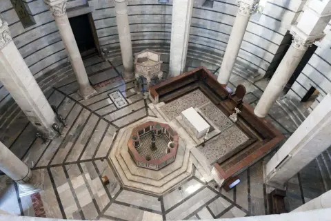 Interno della Torre di Pisa: vista dall'alto del battistero ottagonale, colonne imponenti e mosaici sul pavimento.