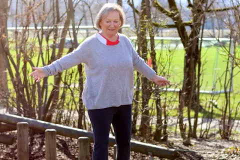 Ältere Frau balanciert auf Holzstämmen im Freien.