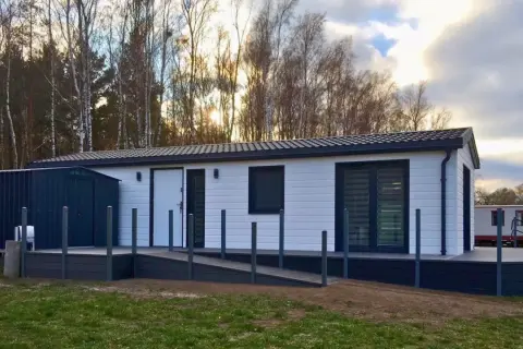 Nowoczesne domki letniskowe przystosowane dla osób niepełnosprawnych, z podjazdem i tarasem, otoczone drzewami.