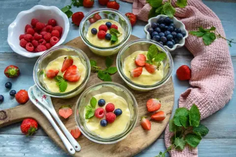 Vier Gläschen cremiger Vanillepudding, garniert mit frischen Erdbeeren, Himbeeren und Blaubeeren. Ein süßer Genuss!