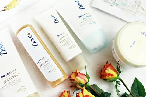 Krem do rąk, olejek i balsam do ciała z serii Dove DermaSpa Goodness, otoczone płatkami róż.