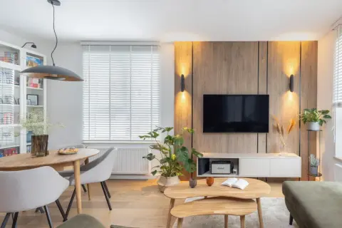 Przytulny salon inspiracje: drewniana ściana z TV, okrągły stół z krzesłami, rośliny i stylowe oświetlenie tworzą ciepłą atmosferę.