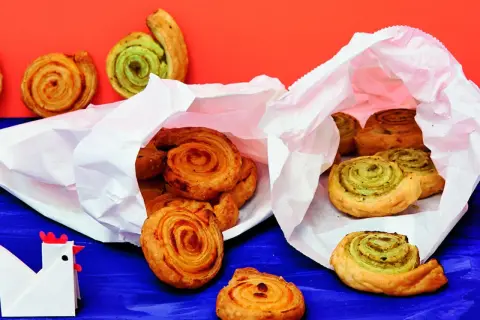 Zwei weiße Papiertüten quellen über mit köstlichen Pesto-Schnecken. Einige sind goldbraun, andere mit grünem Pesto gefüllt.