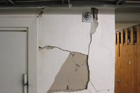 Stora sprickor i väggen visar behovet av att laga sprickor i grunden. En metallplatta med bult sitter fast i den spruckna väggen.