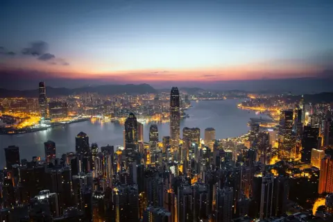 Wieczorny widok na rozświetlony Hongkong. Wiele wieżowców lśni światłami, tworząc niesamowity krajobraz. Ciekawe fakty o tym mieście można odkrywać, podziwiając jego panoramę.