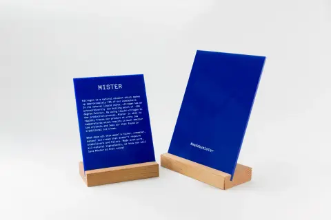 Deux panneaux en **lettre plexiglas** bleus sur des supports en bois. L'un décrit le processus de fabrication de Mister, l'autre affiche le hashtag #madebymister.