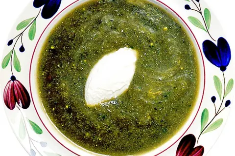 A bowl of green soup with a dollop of cream, garnished with colorful floral patterns.
